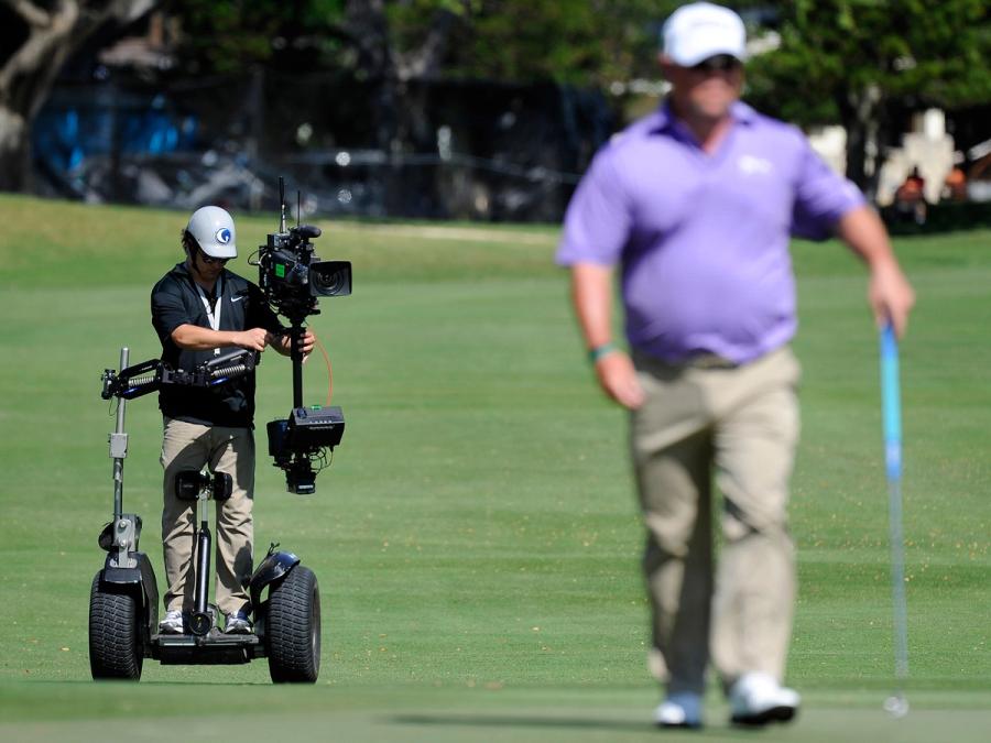 A cameraperson on a Segway rides behind a golfer during a tournament.