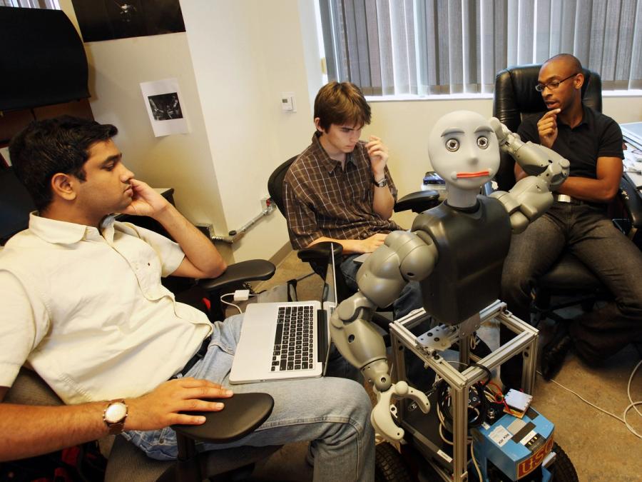 Three people sit around the robot.