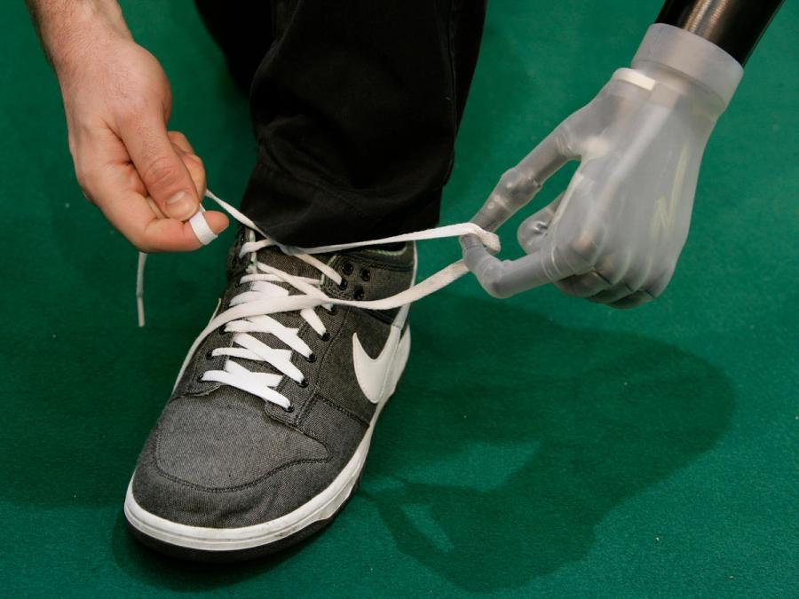 A person ties their shoelaces with their hand and prosthetic hand.