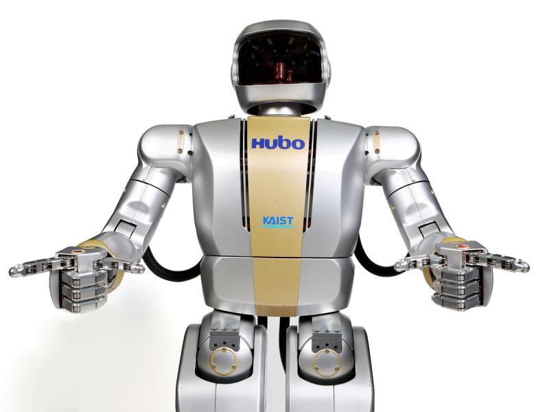 A sleek silver robot with head like an astronauts helmet holds its arms out to the camera. Two fingers are outstretched on each hand, while the other three fingers are clenched.
