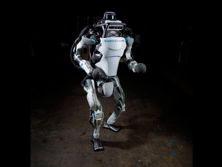 An advanced looking two legged humanoid robot stands on a dark surface.