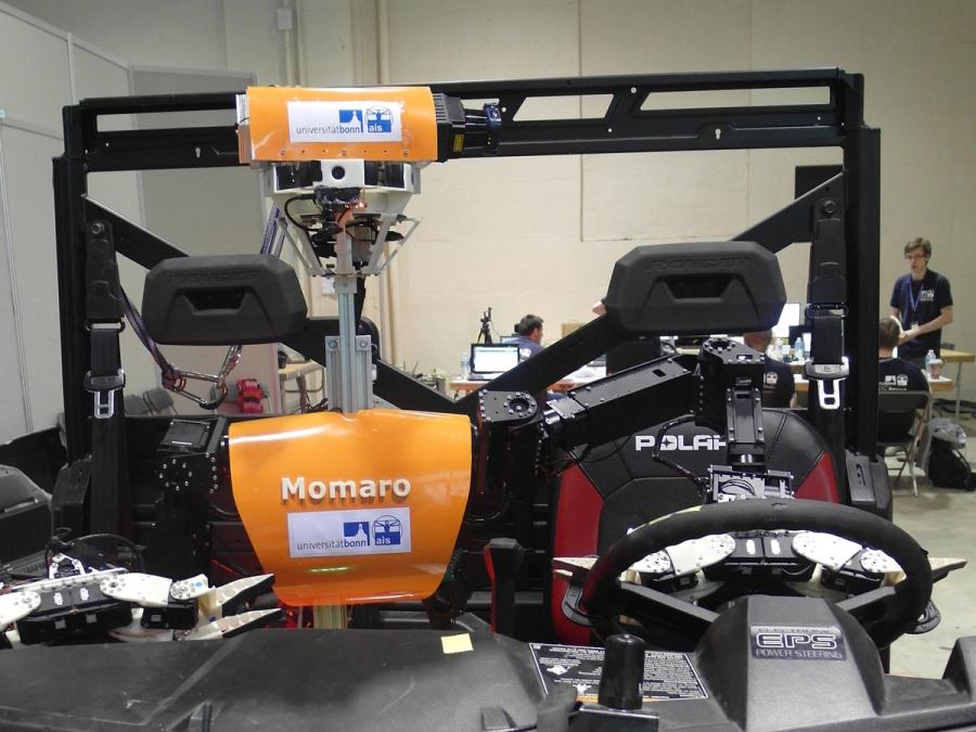 The robots orange torso, neck and head are seen in a cart-like vehicle.