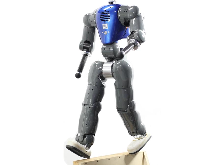 A bipedal robot with a blue torso casing and grey arms and legs walks on a thin wooden plank.