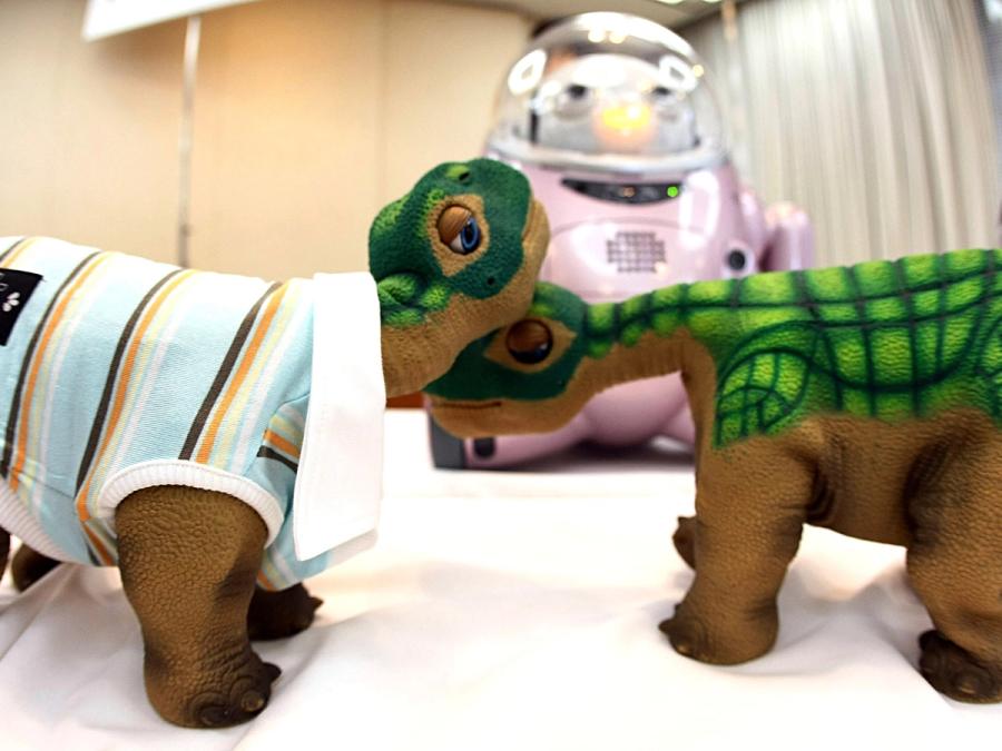 Two Pleo robots nuzzle each other on a table.