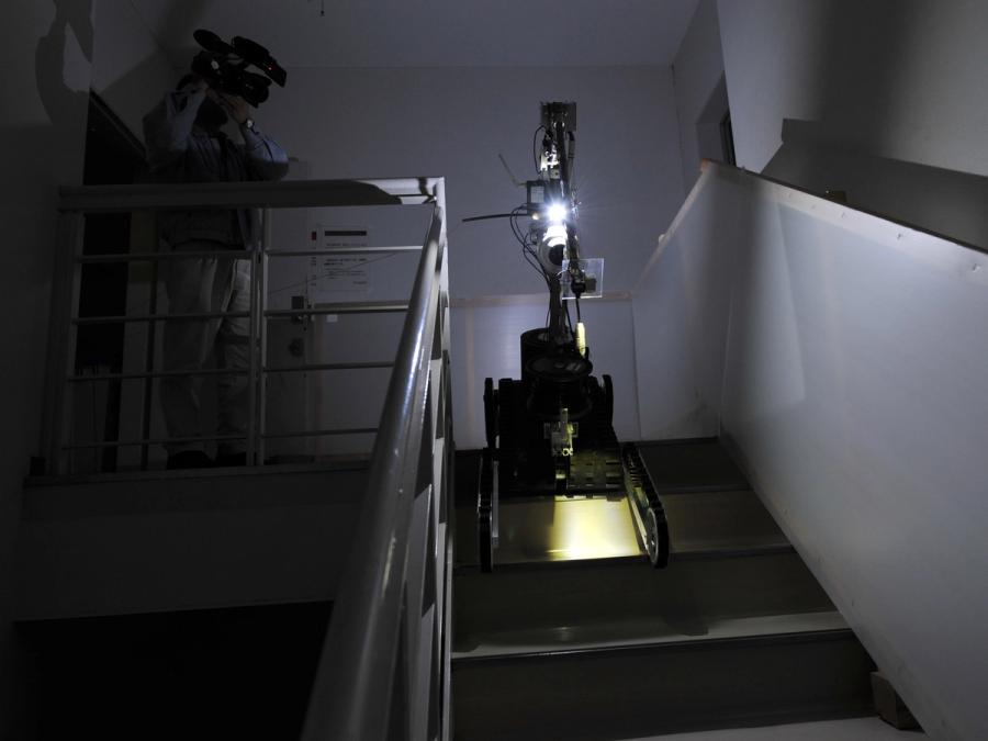 The robot shines a light downward as it rolls down stairs in a dark building stairwell.