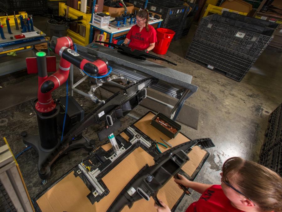 Two people and one Sawyer robot work together in a factory.