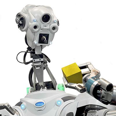 Close up of a humanoid robot looking at a yellow block held in its grip.