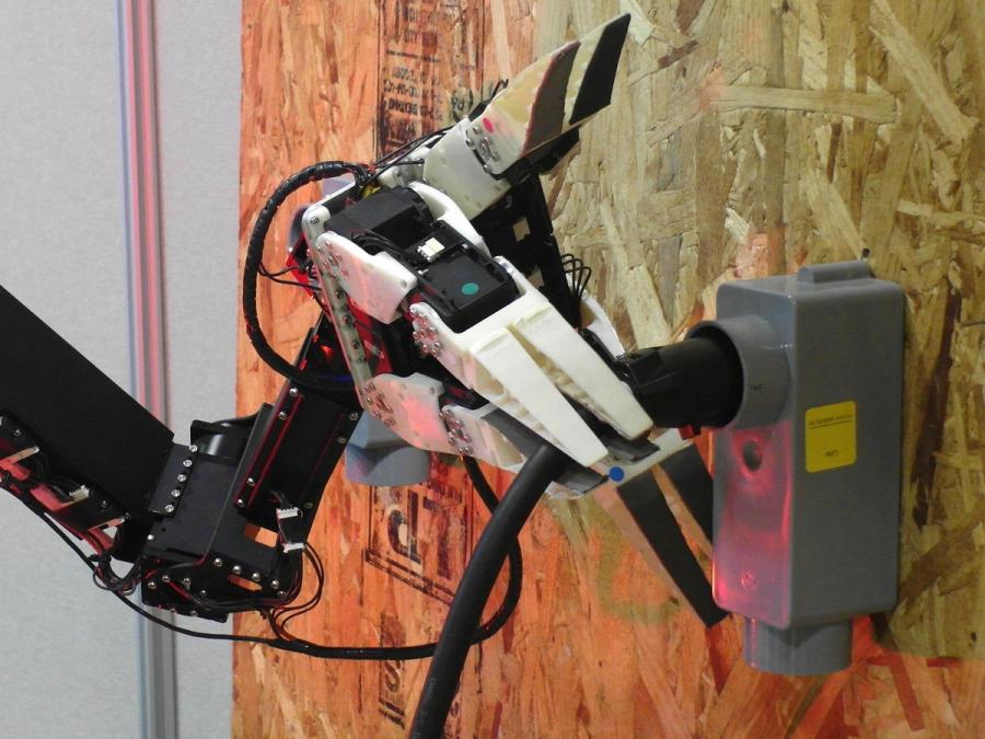Close-up of the robots grippers holding a plug in a wall.