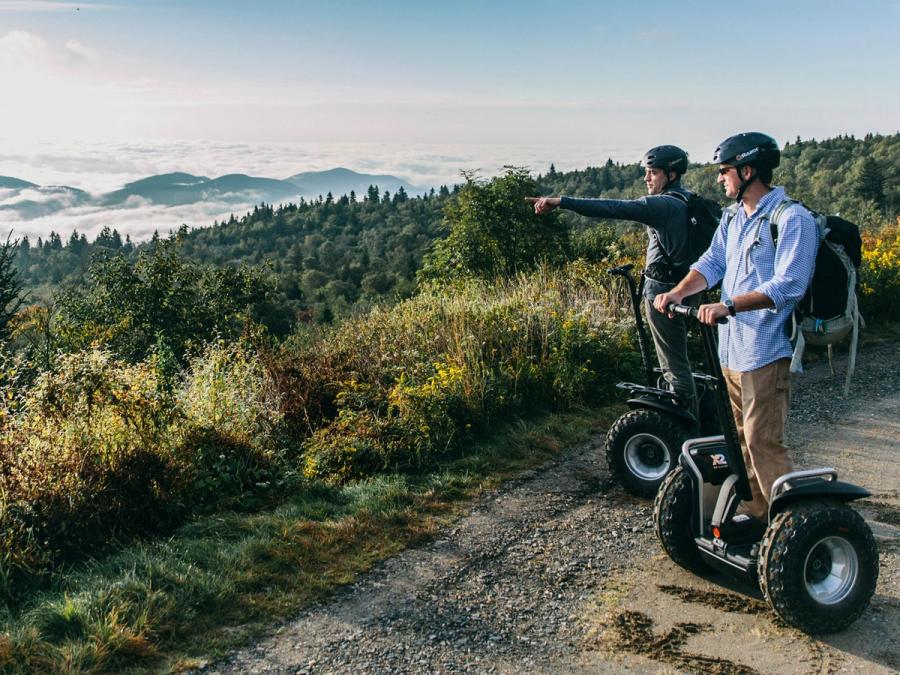 Two people on Segways with thick all-terrain wheels look out over a scenic vista.