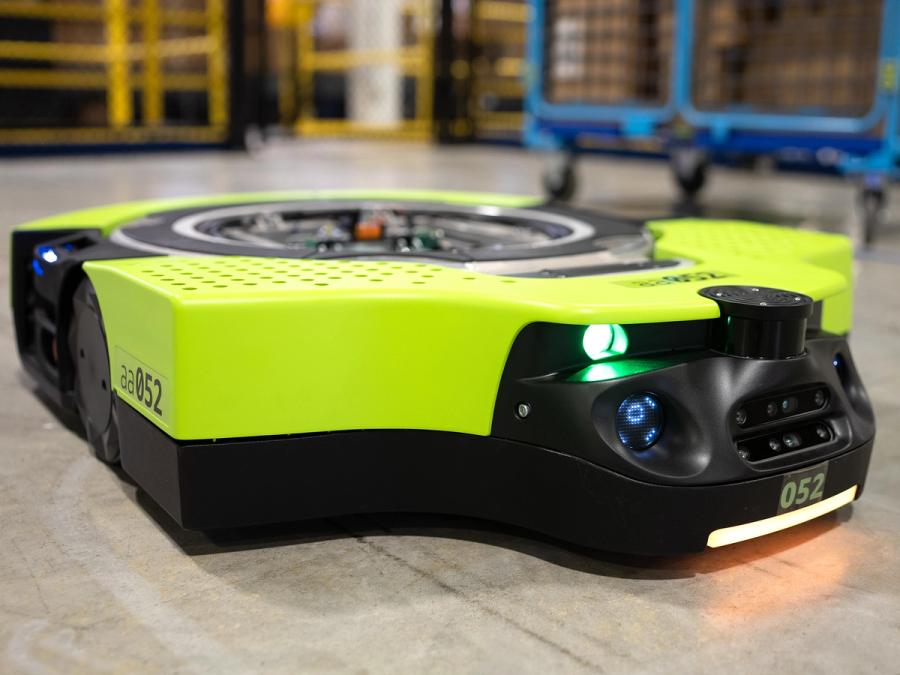 A green mobile robot on the floor of a warehouse.