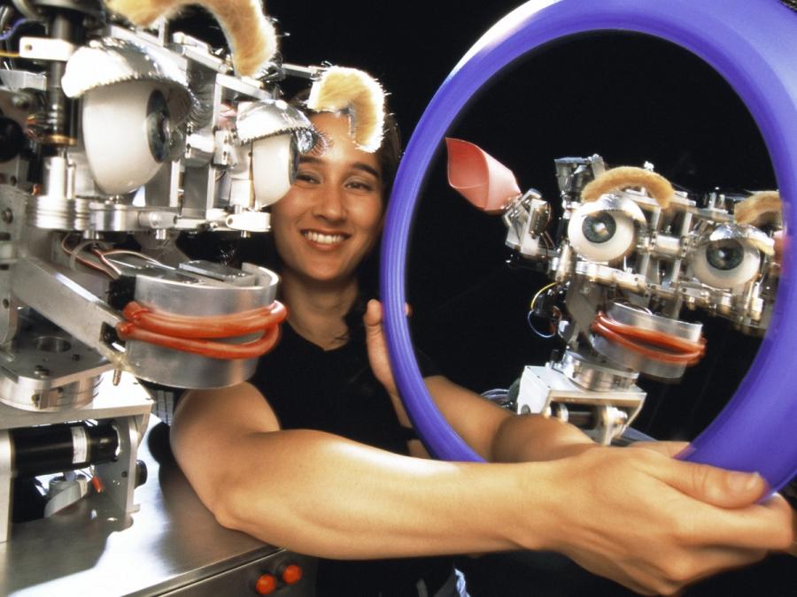 A smiling woman shows the robot its own smiling reflection.