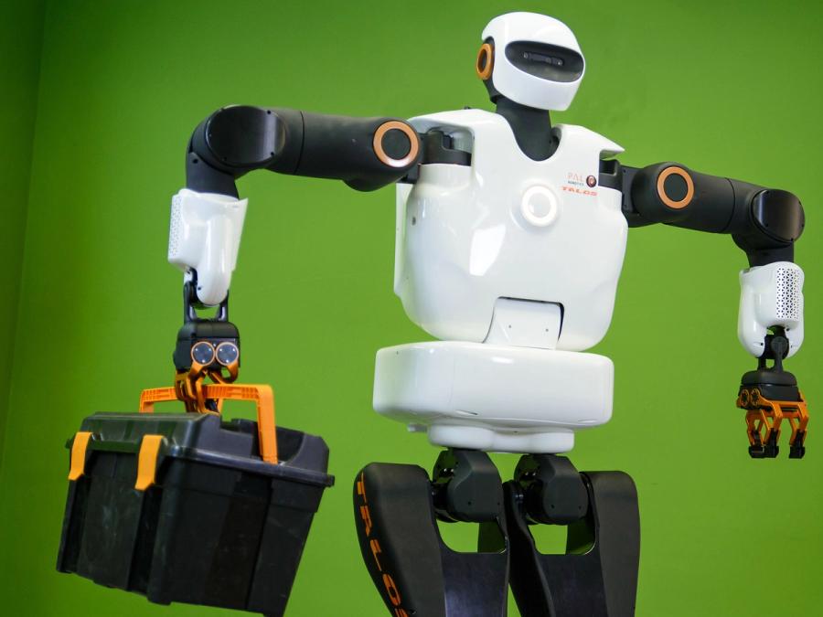 A white and black humanoid robot holds a toolbox in one of its gripper hands.