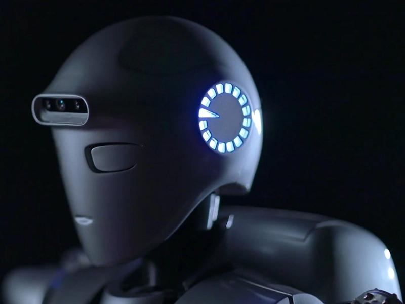 Close-up of a grey humanoid's head with a shiny wheel of light and a row of cameras and sensors.