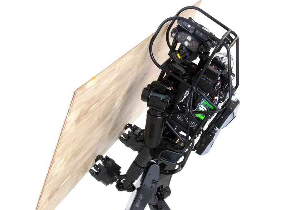 A sleek black humanoid robot carries a large wood sheet.