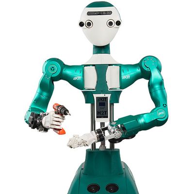 A humanoid robot with a white face and shiny green torso and arms holds an orange drill.