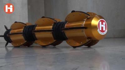 A robotic snake with a body of golden metal and dark rubber flexible tube slithers on a concrete floor.