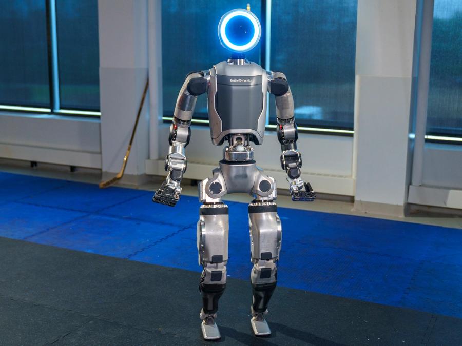 Boston Dynamics' Atlas robot, a grey and silver bipedal robot with a circular head that glows blue, and long arms and gripper hands.