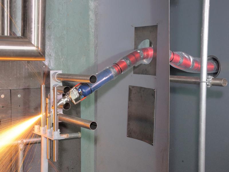A red, snake-like segmented robot is piped through a hold in a wall. Fiery sparks are directed out of it's triangular front piece.