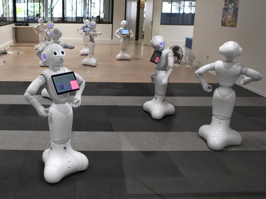 Nine pepper robots are seen in a large room posed in different ways.