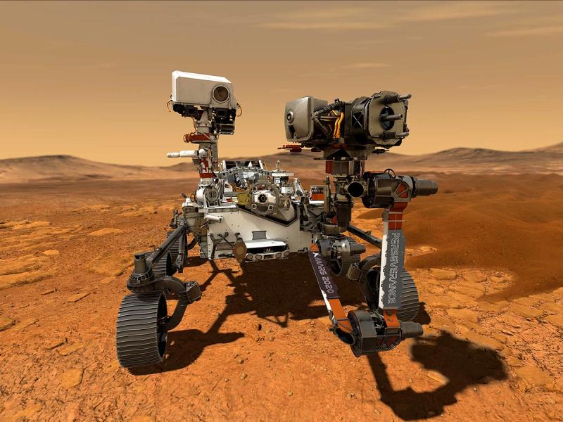 A car-sized rover with tracked wheels, a base covered in scientific equipment, and robotic arms with tools and multiple cameras sits on a red barren planet.