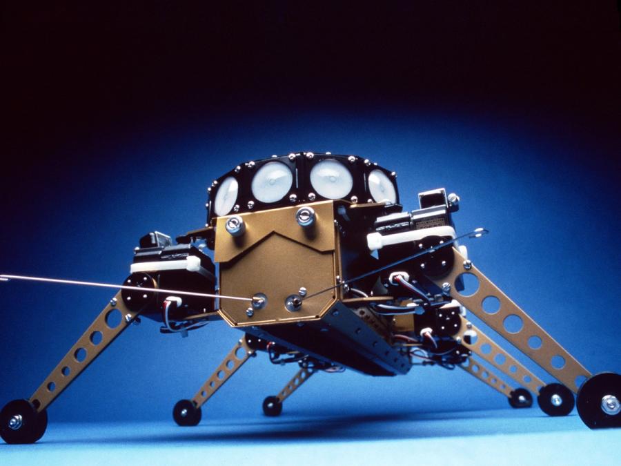 An older model of the robot with six golden wheeled legs, a gold rectangular body and a circular piece on top.