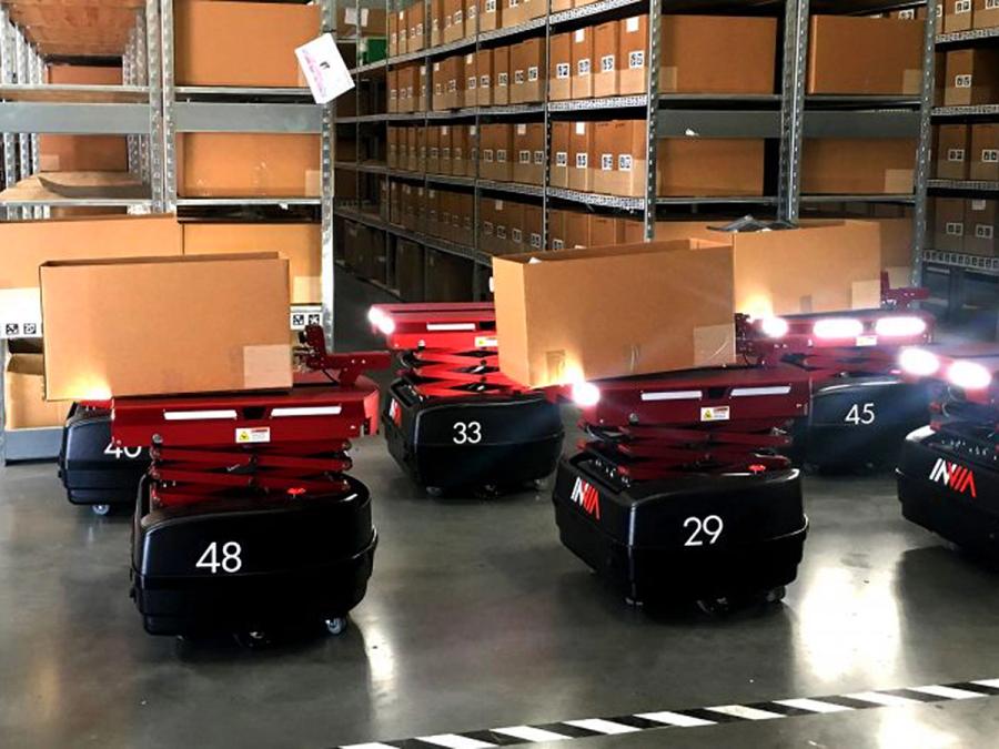 Multiple Picker Robots glow as they carry boxes through a warehouse space.