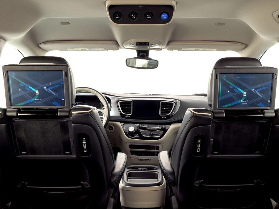 A backseat view of interior of car with screens on the back of the front seat rest which show an image of the car move through a grid of roads.