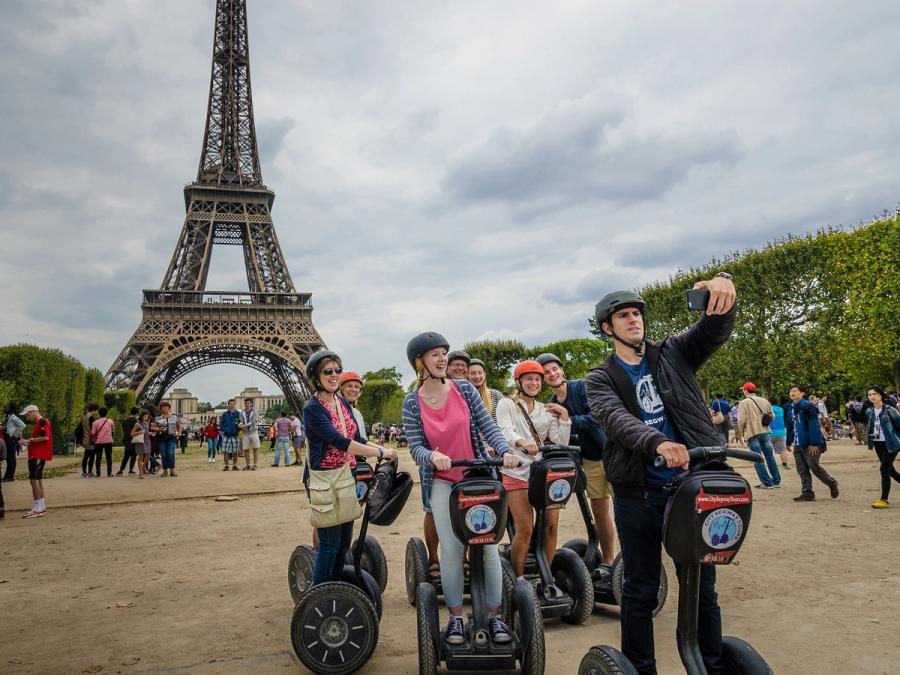 A person on a Segway takes a selfie with a group of Segway riders in front of the Eiffel Tower.