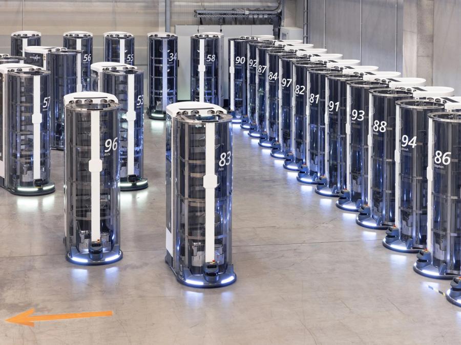 A warehouse with a line of mobile robots, and many others on the move.