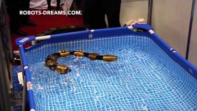 A robotic snake with a metal body swims in a small plastic pool at a trade show.