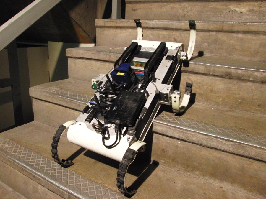 A white robotic hexapod with electronics on its base goes up a set of stairs.