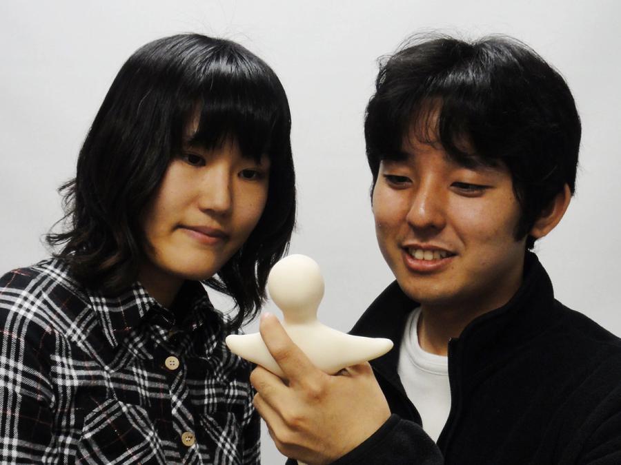 Two people look at a mini Telenoid, which fits in the palm of a hand.