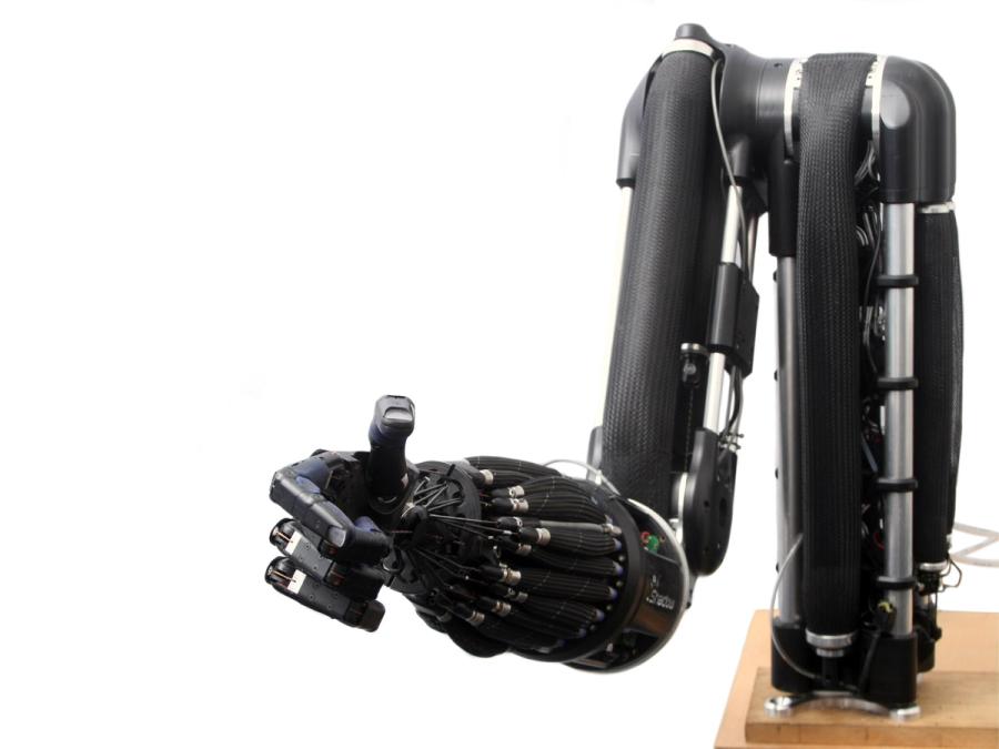 A high-tech black prosthetic hand is attached to a tabletop black robotic arm system.