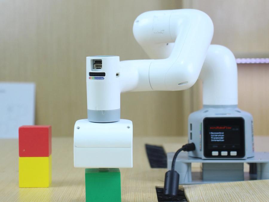 The myCobot 280 white robot arm picks up a green black on a table which also has a red and a yellow block.