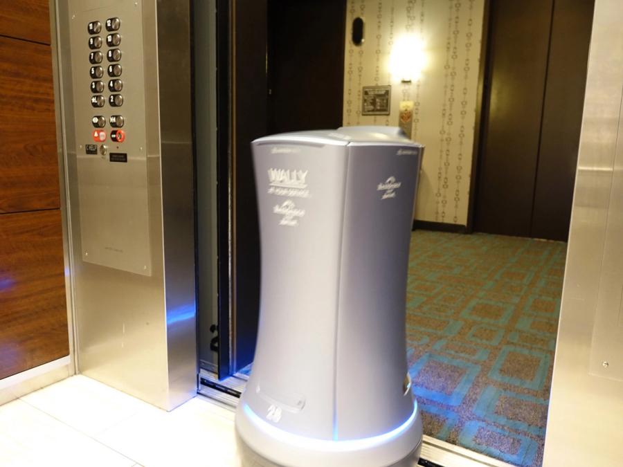 A cylindrical delivery robot gets out of an elevator.