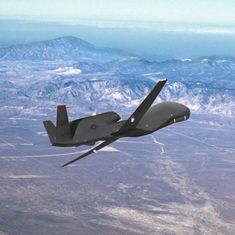 A military drone the size and shape of an airplane flies over mountains.