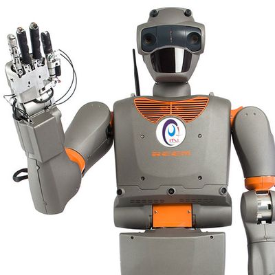 A grey and orange humanoid waves at the camera. It has a cartoonish head with eyes and a plate over its mouth area.