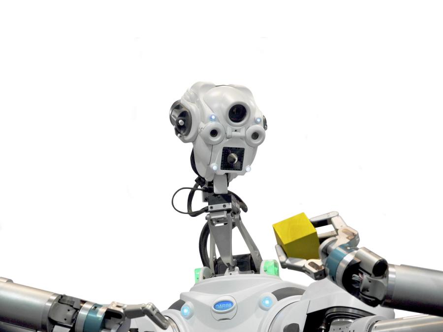 Close up of a humanoid robot looking at a yellow block held in its grip.