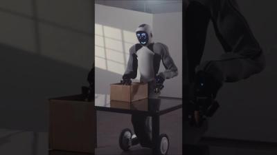 Humanoid robot EVE, with LED face, fabric covered arms, and wheeled legs, picks up a cardboard box from a desk on a mock home.