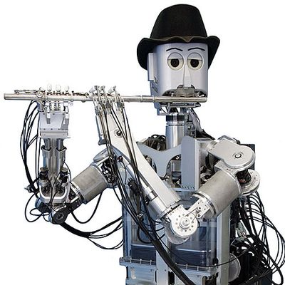 A silver humanoid robot whose frame includes many black wires wears a black hat and plays a flute against a white background.