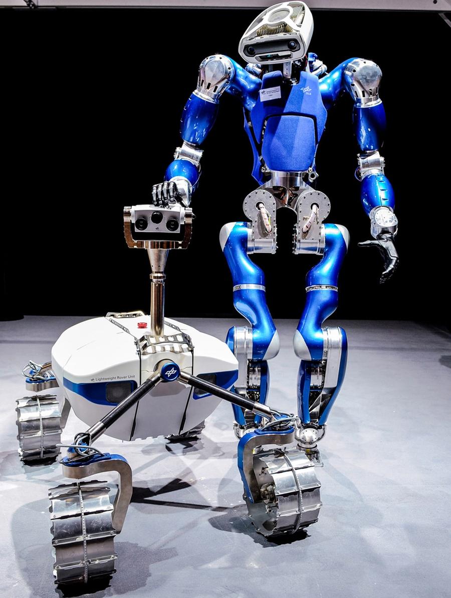 A shiny blue and silver bipedal humanoid rests a hand on the top of a rugged space rover.