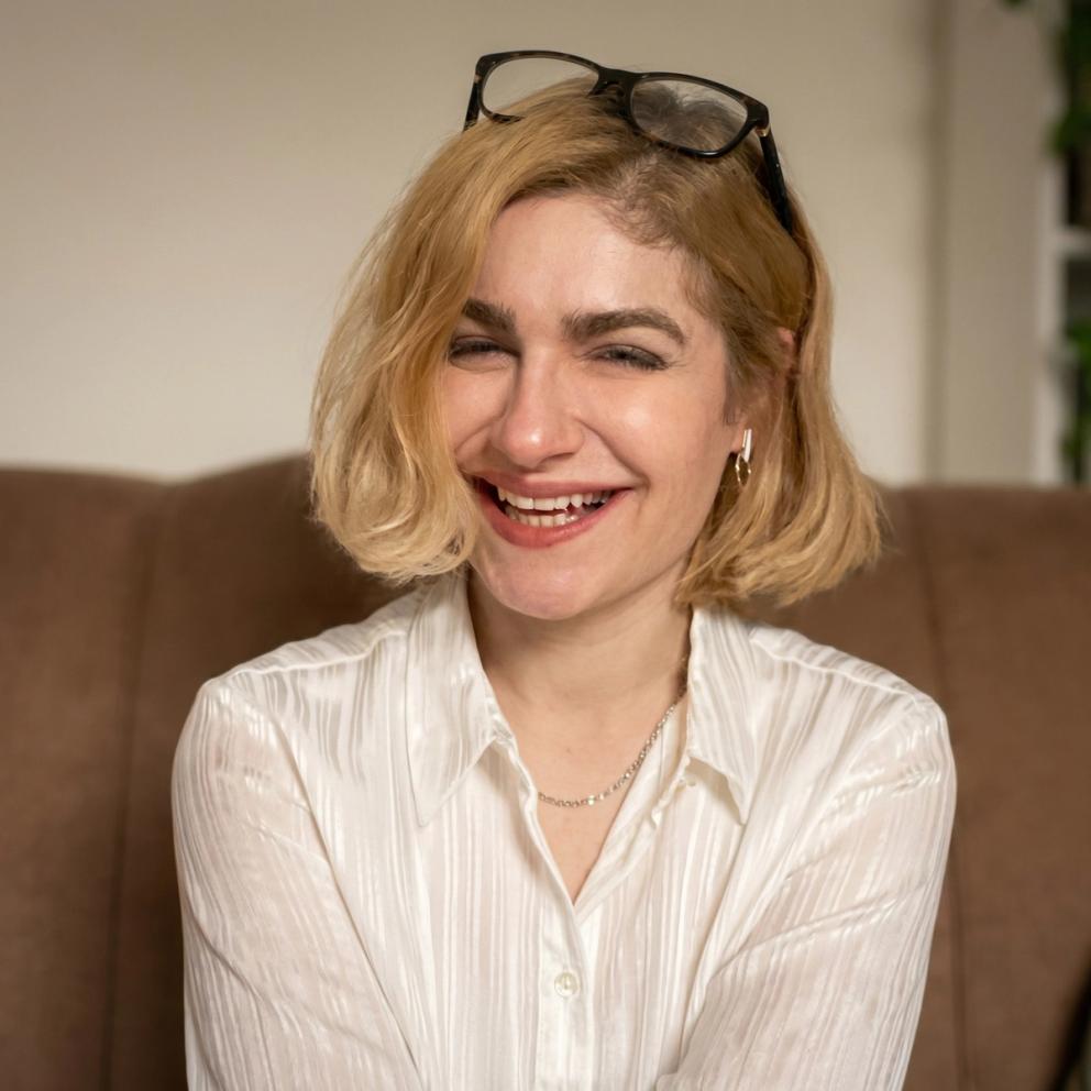 A woman with short blonde hair and glasses on her head smiles at the camera