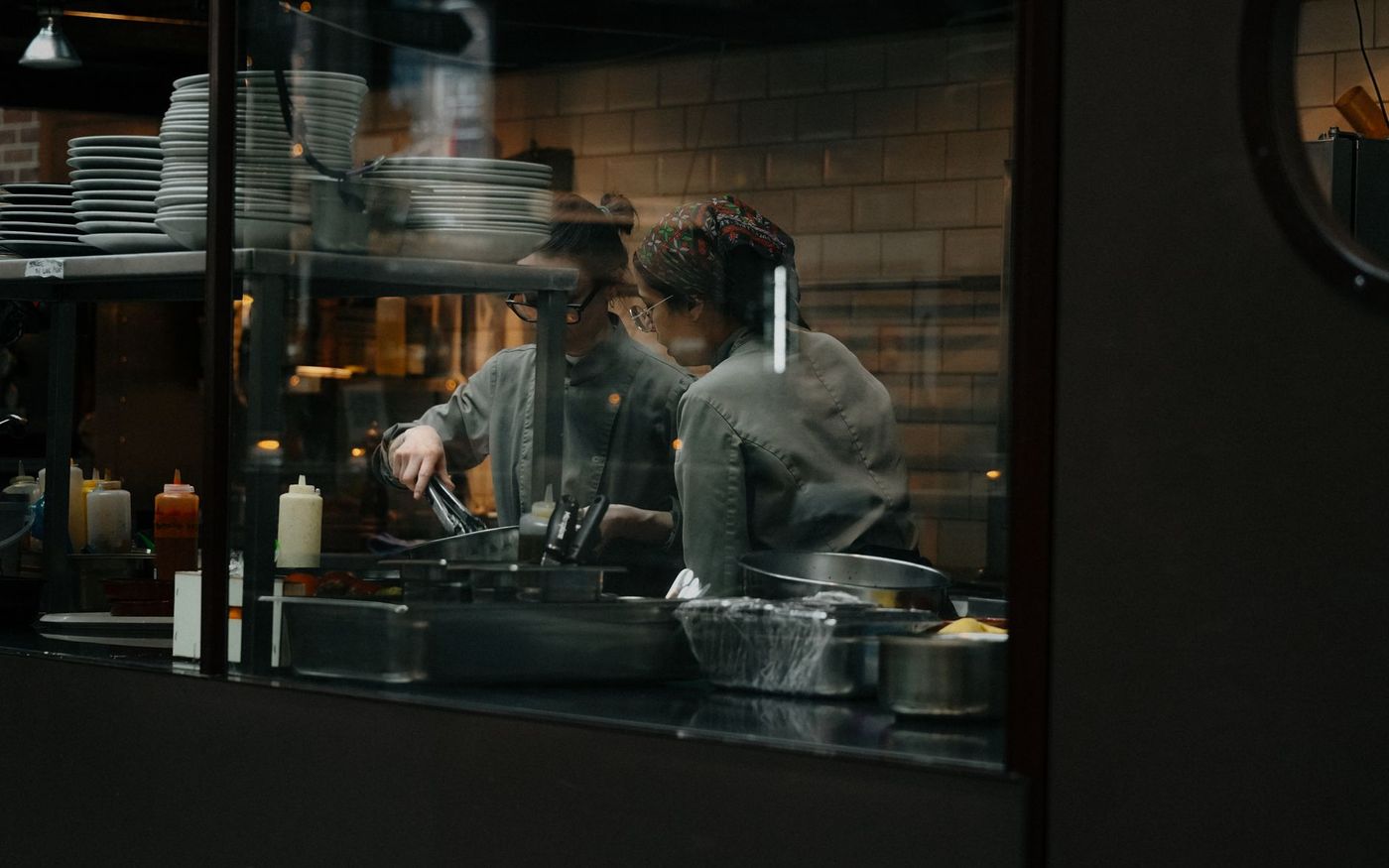 Gestor de restaurante confere uma escala de trabalho enquanto a equipe atua na cozinha. — Foto: Mathias Reding (Pexels)