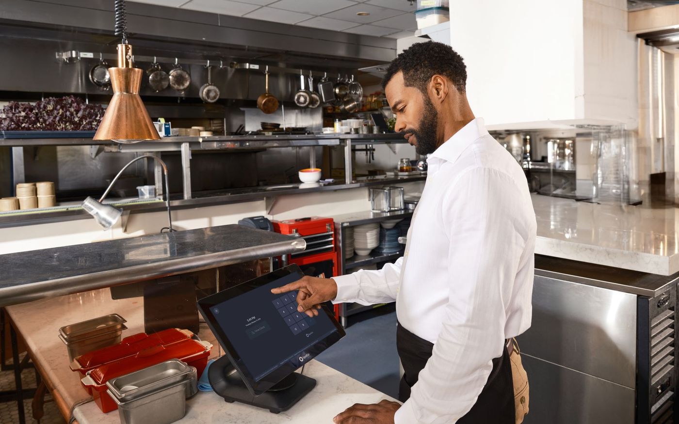 Gestor de restaurante confere registros de operação enquanto a equipe trabalha na cozinha. — Foto: SpotOn POS (Pexels)