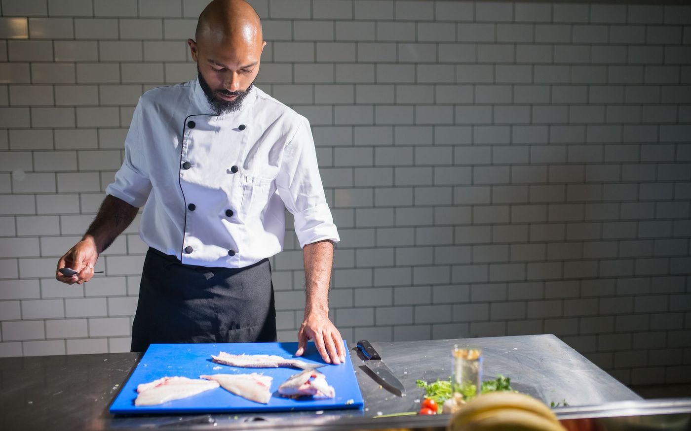 Chef porciona filés de pescado em uma cozinha profissional enquanto a equipe prepara os ingredientes. — Foto: Kampus Production (Pexels)