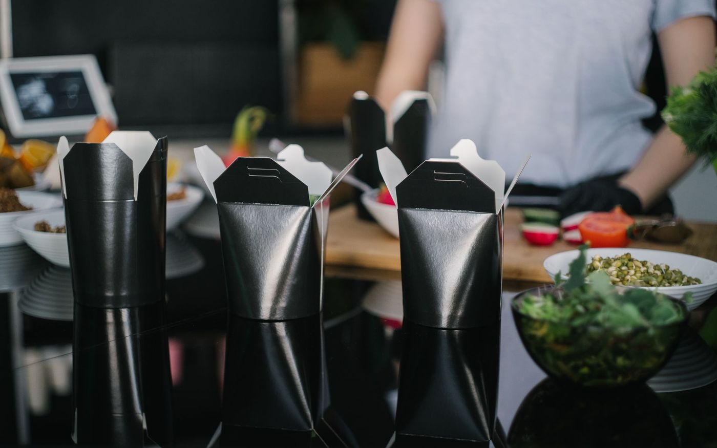 Gestor de restaurante analisa um prato e uma embalagem para viagem em uma mesa próxima à cozinha. — Foto: Mikhail Nilov (Pexels)