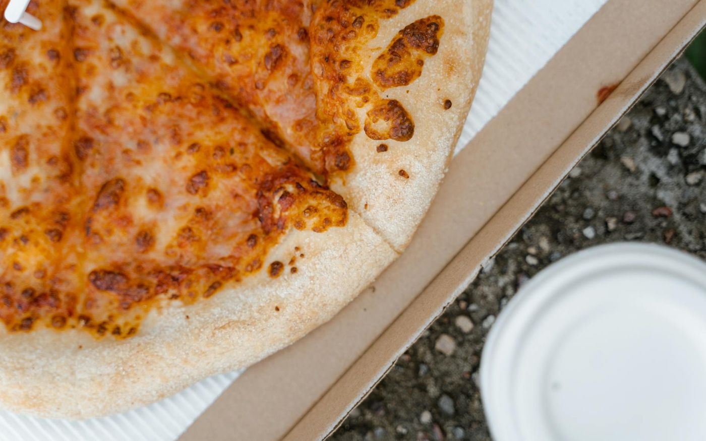 Drone entregando pizza em área urbana ao entardecer, com letreiro de restaurante ao fundo. — Foto: MART  PRODUCTION (Pexels)