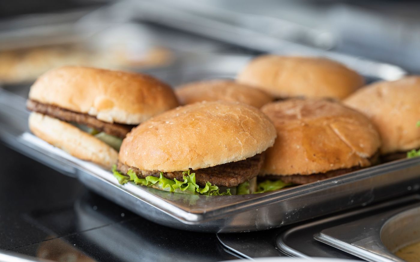 Cozinheiro monta um hambúrguer em uma cozinha profissional enquanto a operação segue durante o serviço. — Foto: Engin Akyurt (Pexels)
