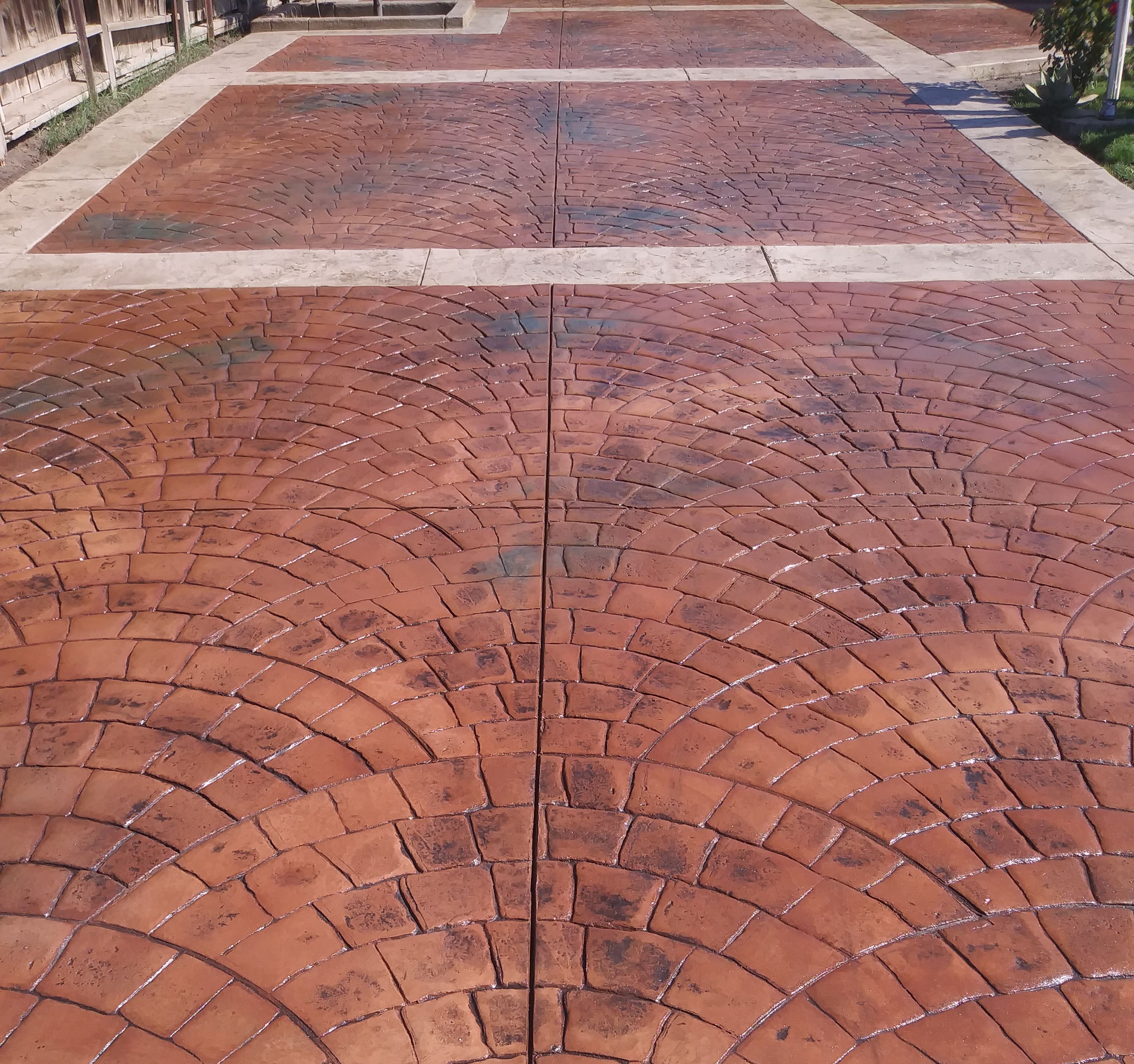 Decorative stamped concrete featuring a reddish fan-pattern design with textured stone-like borders.