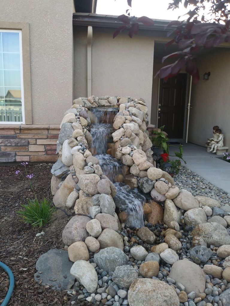 Multi-tier natural stone waterfall with river rock landscaping at front entry